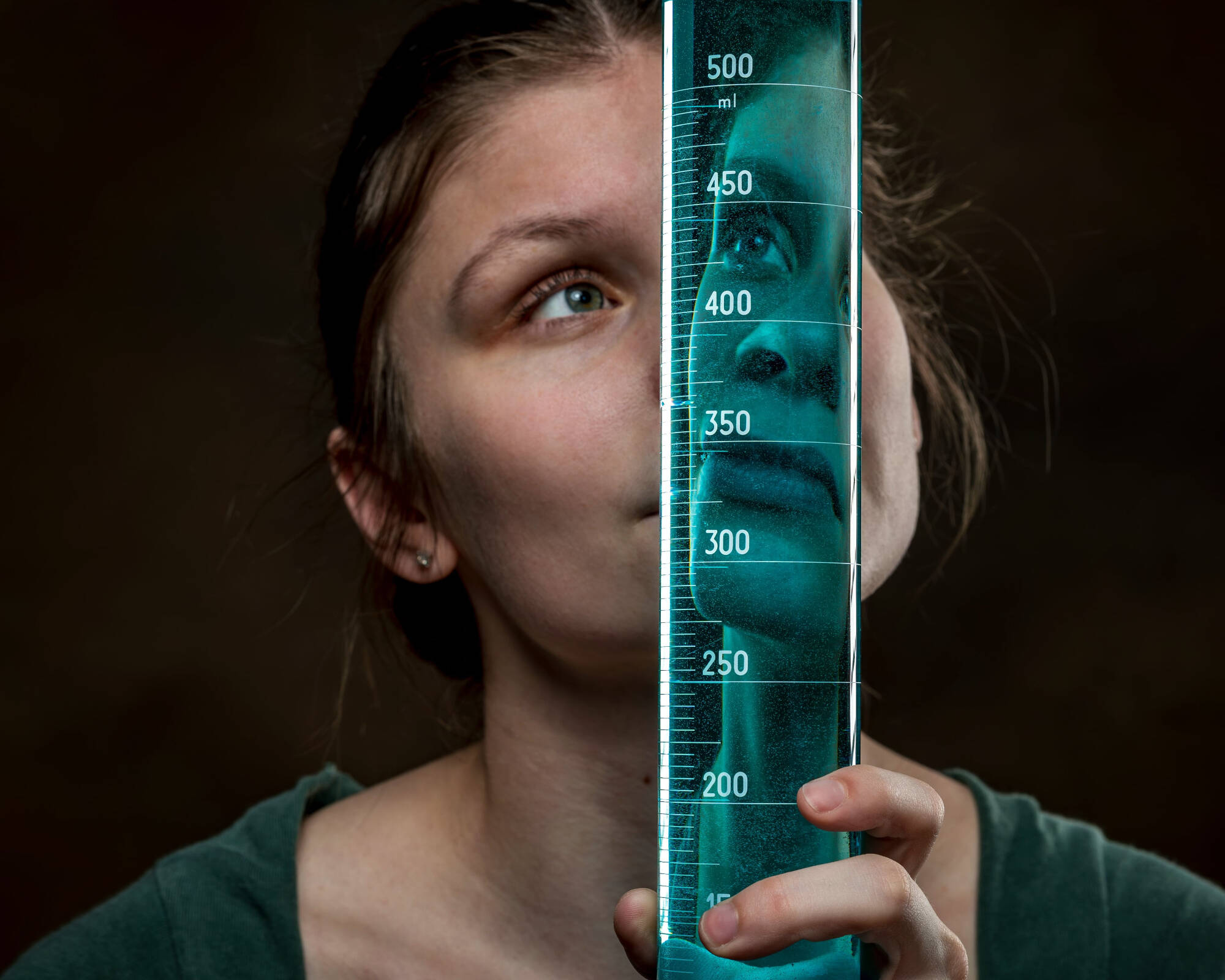 Student scholar Lilly Helsel looks through a beaker, with half her face reflected in the beaker
